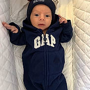 Jack is registered to the contest to win money with this photo: baby, infant, onesie, navy_blue, beanie, hat, clothing, face, head, person, quilted, white, bed, hand, newborn, sleeping_area, cute, portrait, babywear, soft