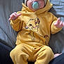 Arlo joined the competition — help win amazing prizes! baby, child, pacifier, yellow_clothing, lion_king, hat, knit_hat, socks, sitting, person, indoor, gray_background, cute, infant, portrait, face, hands, feet, soft_fabric, lap