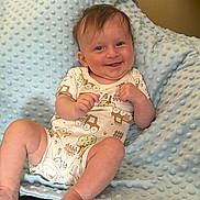 Arlo is registered to the contest to win money with this photo: baby, smiling, onesie, blue_blanket, infant, happy, face, person, child, soft_texture, cute, indoors, skin, hand, foot, sitting, expression, comfort, background, closeup