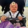 Mia is registered to the contest to win money with this photo: baby, smiling, stroller, headband, flower, blanket, cozy, clothing, hands, outdoor, sunlight, seatbelt, child, cute, pink, purple, knitted, happy, portrait, person