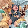 baby, infant, smiling, batman_onesie, hooded_clothing, plush_toys, teddy_bear, giraffe_toy, dinosaur_toy, triceratops_toy, milestone_card, 3_months, blanket, socks, happy, cute, indoors, soft_toys, child, portrait