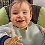 Nolann a rejoint le concours — aidez-le/la à gagner de superbes lots ! toddler, child, high_chair, bib, smock, food, messy, hand, happy, smile, indoor, bookshelf, curtain, face, person, feeding, baby, clothing, table, expression