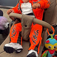 Drayton-Reign is registered to the contest to win money with this photo: baby, stroller, orange_hoodie, orange_pants, white_shoes, laughing, happy, child, toy, plush_toy, outdoor, pavement, seatbelt, casual_clothing, person, infant, smile, curly_hair, footwear, daylight