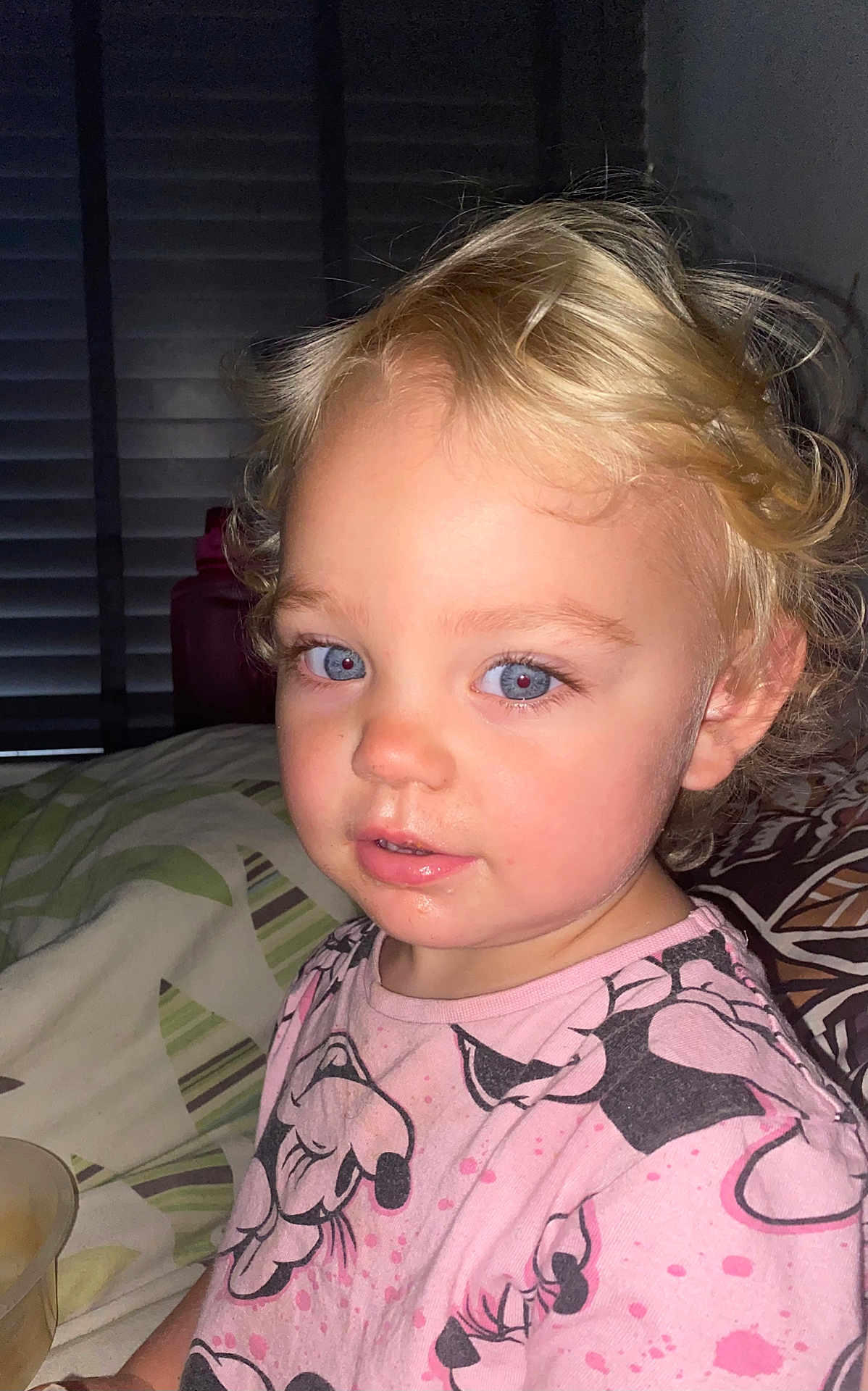 Kyra joined the competition — help win amazing prizes! toddler, child, blonde_hair, blue_eyes, curly_hair, pink_shirt, cartoon_print, indoor, bed, blanket, face, portrait, person, curious_expression, messy_face, flash_photography, young_child, sitting, closeup, casual_clothing