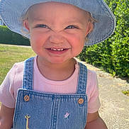 Kyra is registered to the contest to win money with this photo: child, toddler, smiling, denim_hat, denim_overalls, pink_shirt, outdoor, sunny, grass, sidewalk, greenery, face, happy, cute, daylight, portrait, young_child, blue_sky, casual_clothing, animal_patch