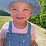 child, toddler, smiling, denim_hat, denim_overalls, pink_shirt, outdoor, sunny, grass, sidewalk, greenery, face, happy, cute, daylight, portrait, young_child, blue_sky, casual_clothing, animal_patch