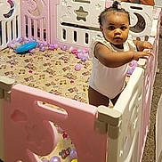 Kimber is registered to the contest to win money with this photo: toddler, child, playpen, pink, white, plastic_balls, patterned_mat, indoor, carpet, baby, person, standing, curious, looking_at_camera, home, furniture, toys, cute, infant, play_area