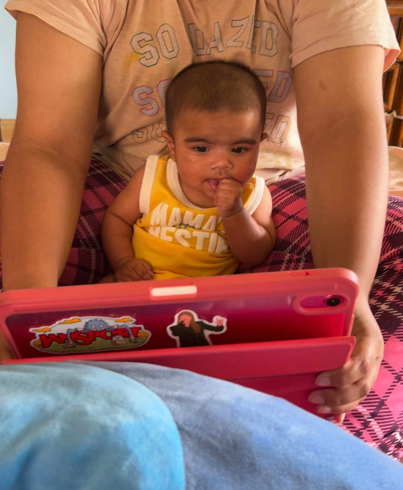 Waziya is registered to the contest to win money with this photo: baby, child, tablet, adult, hands, yellow_shirt, plaid_pants, indoor, curious, technology, face, person, sitting, holding, arm, close_up, home, furniture, skin, expression