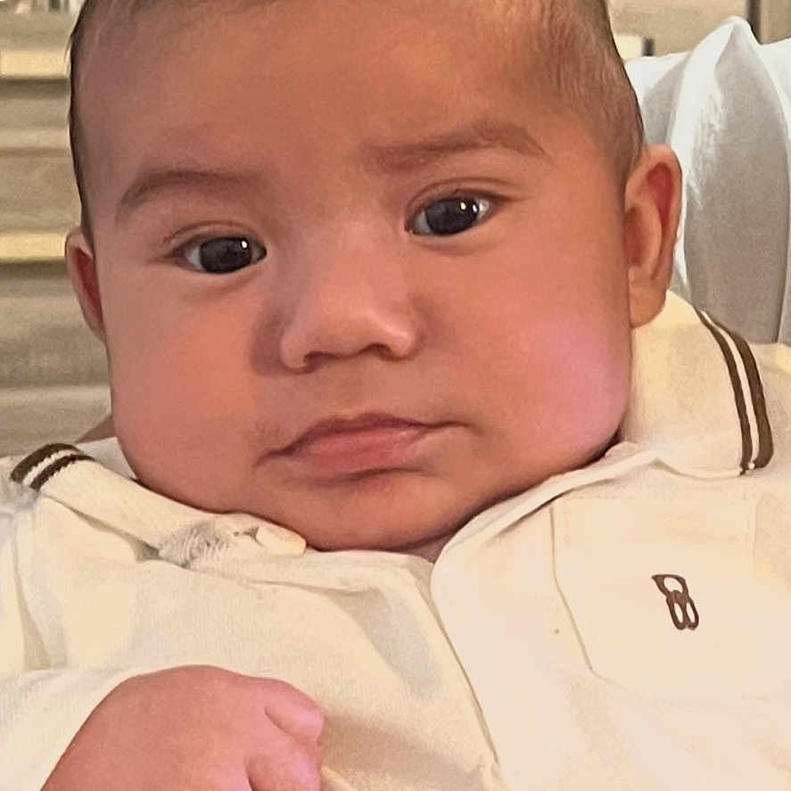 Esekiele a rejoint le concours — aidez-le/la à gagner de superbes lots ! baby, background, child, close_up, cute, eyebrows, face, furniture, hair, hand, head, indoor, infant, portrait, room, serious_expression, sitting, skin, white_clothing, young_child