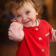 Aurore participe au concours pour gagner de l'argent avec cette photo : toddler, child, smiling, curly_hair, red_jacket, toy_phone, indoors, portrait, happy, cute, buttoned_jacket, face, person, warm_lighting, expression, young_child, casual_clothing, closeup, playful, joyful