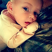 Cheyenne is registered to the contest to win money with this photo: baby, child, infant, portrait, close_up, face, eyes, smiling, curious, sitting, lying_down, hand, fist, hoodie, clothing, blanket, bed, indoors, cozy, photography
