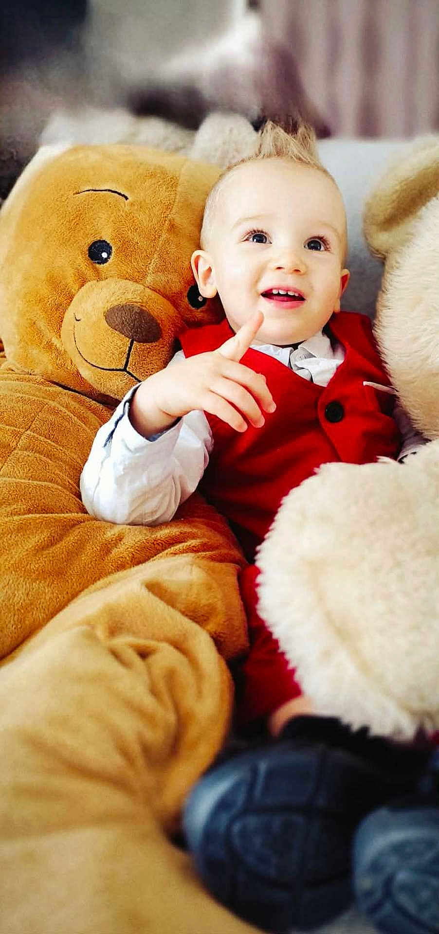 Léo participe au concours pour gagner de l'argent avec cette photo : child, toddler, smiling_child, pointing, teddy_bear, stuffed_animal, plush_toy, red_vest, white_shirt, formal_wear, indoor, couch, portrait, closeup, joyful, blond_hair, spiky_hair, shoe, cozy, seated