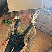 Malia a rejoint le concours — aidez-le/la à gagner de superbes lots ! child, cardboard_box, curly_hair, denim_overalls, long_sleeve_shirt, indoor, kitchen, floor, window, light, playful, standing, casual_clothing, looking_sideways, young_child, smile, curiosity, home, person, footwear