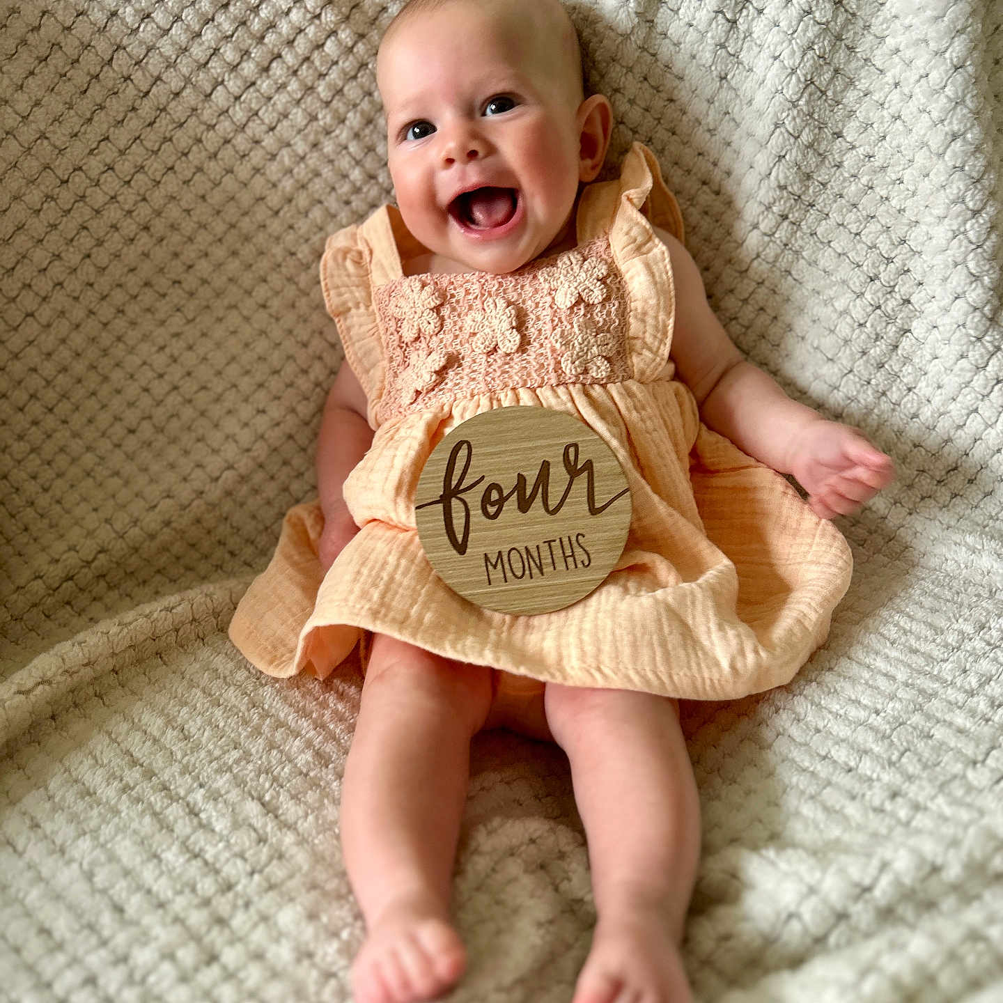 Madelyn is registered to the contest to win money with this photo: baby, blanket, child, cute, dress, face, feet, four_months, hand, happy, indoors, infant, peach, portrait, sitting, skin, smile, texture, wooden_sign, young