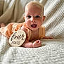 Madelyn joined the competition — help win amazing prizes! baby, infant, smiling, four_months, blanket, peach_outfit, wooden_sign, closeup, cute, happy, portrait, child, lying_down, soft_texture, indoors, face, head, skin, eyes, mouth