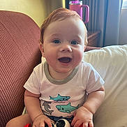 Liam joined the competition — help win amazing prizes! baby, child, smile, happy, toy, crab_toy, indoor, chair, cushion, lamp, water_bottle, curtains, window, person, clothing, short_sleeve_shirt, red_hair, cute, playful, portrait