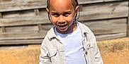 Noah a rejoint le concours — aidez-le/la à gagner de superbes lots ! child, boy, smiling, cornrows, white_shirt, beige_jacket, jeans, outdoor, fence, sunlight, shadow, playful, casual_clothing, person, portrait, daylight, concrete, young, fashion, happy