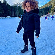 Noah participe au concours pour gagner de l'argent avec cette photo : child, snow, winter_clothing, boots, curly_hair, smiling, outdoor, mountains, pine_trees, forest, daylight, cold_weather, scenic, people, walking, nature, happy, landscape, blue_sky, snowy_ground