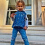 child, denim_vest, jeans, sneakers, stairs, building, chocolate_bar, braided_hair, beads, smiling, outdoor, casual_clothing, person, fashion, playful, sunlight, modern_architecture, steps, young_child, portrait