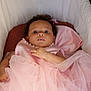 baby, infant, pink_dress, pearls, curly_hair, bassinet, cushion, soft_fabric, portrait, close_up, child, sleeping_area, cute, face, hand, indoors, cozy, tulle, newborn, looking_up