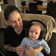 Aleksander participe au concours pour gagner de l'argent avec cette photo : baby, woman, headphones, tattoos, indoor, couch, smile, curious, child, holding, person, furniture, dining_table, chair, water_bottle, home, casual, expression, cute, family