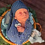 newborn, baby, blue_wrap, knit_hat, sleeping, basket, heart_prop, blanket, greenery, soft_focus, portrait, infant, cute, peaceful, indoors, warm_lighting, cozy, wrapped, tiny_hand, resting