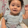 Fiorella is registered to the contest to win money with this photo: baby, bed, bird_illustration, blue_outfit, cherry_blossoms, child, curly_hair, cute, decorative_wall, flower_embroidery, hair_clip, happy, heart_pattern, indoors, infant, pink_hearts, portrait, sitting, smiling, waving