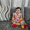 baby, child, couch, curly_hair, curtain, cute, dress, fruit, gray_couch, holding, home, indoor, lemon, looking, patterned_dress, person, pillow, red_booties, sitting, toddler