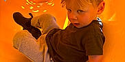 Tate is registered to the contest to win money with this photo: active, blond_hair, boots, casual_clothing, child, curious, cute, expression, fun, hand, indoor, orange, play, playground, portrait, sitting, slide, toddler, yellow, young