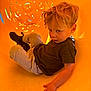 active, blond_hair, boots, casual_clothing, child, curious, cute, expression, fun, hand, indoor, orange, play, playground, portrait, sitting, slide, toddler, yellow, young