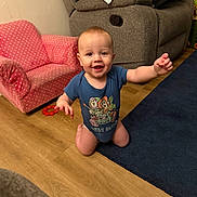 Stetson joined the competition — help win amazing prizes! baby, child, infant, smiling, happy, kneeling, indoor, living_room, portrait, face, blue_shirt, onesie, toy, armchair, sofa, car_seat, rug, wooden_floor, home, sitting