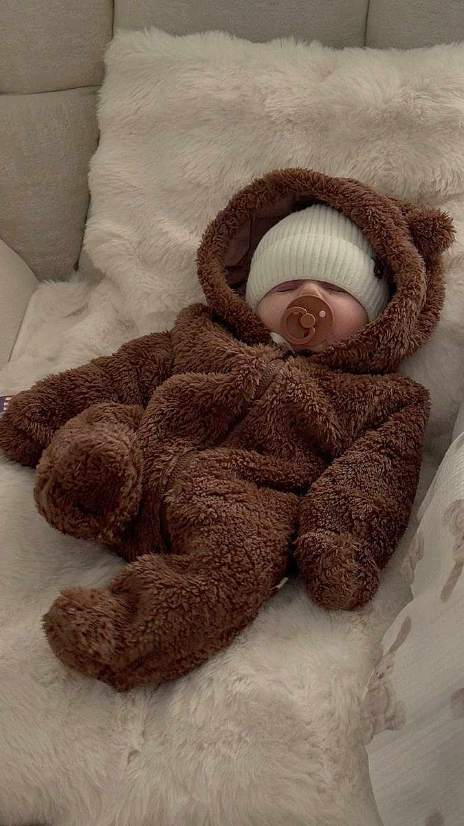 Amaya is registered to the contest to win money with this photo: baby, infant, sleeping, pacifier, bear_suit, hood, knit_hat, white_blanket, fuzzy_clothing, soft_texture, cute, cozy, indoor, couch, plush, child, warm, relaxed, face, person