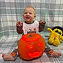 baby, child, pumpkin, jack_o_lantern, halloween, plush_toy, yellow_toy, pajamas, smiling, sitting, blanket, carved_pumpkin, glowing, indoor, cute, festive, happy, orange, face, toy