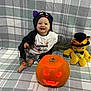 Dominic Nicolas is registered to the contest to win money with this photo: baby, halloween, pumpkin, carved_pumpkin, glowing, plush_toy, hat, smiling, plaid_blanket, costume, child, indoors, cute, orange, black_clothing, toy, happy, sitting, decor, festive