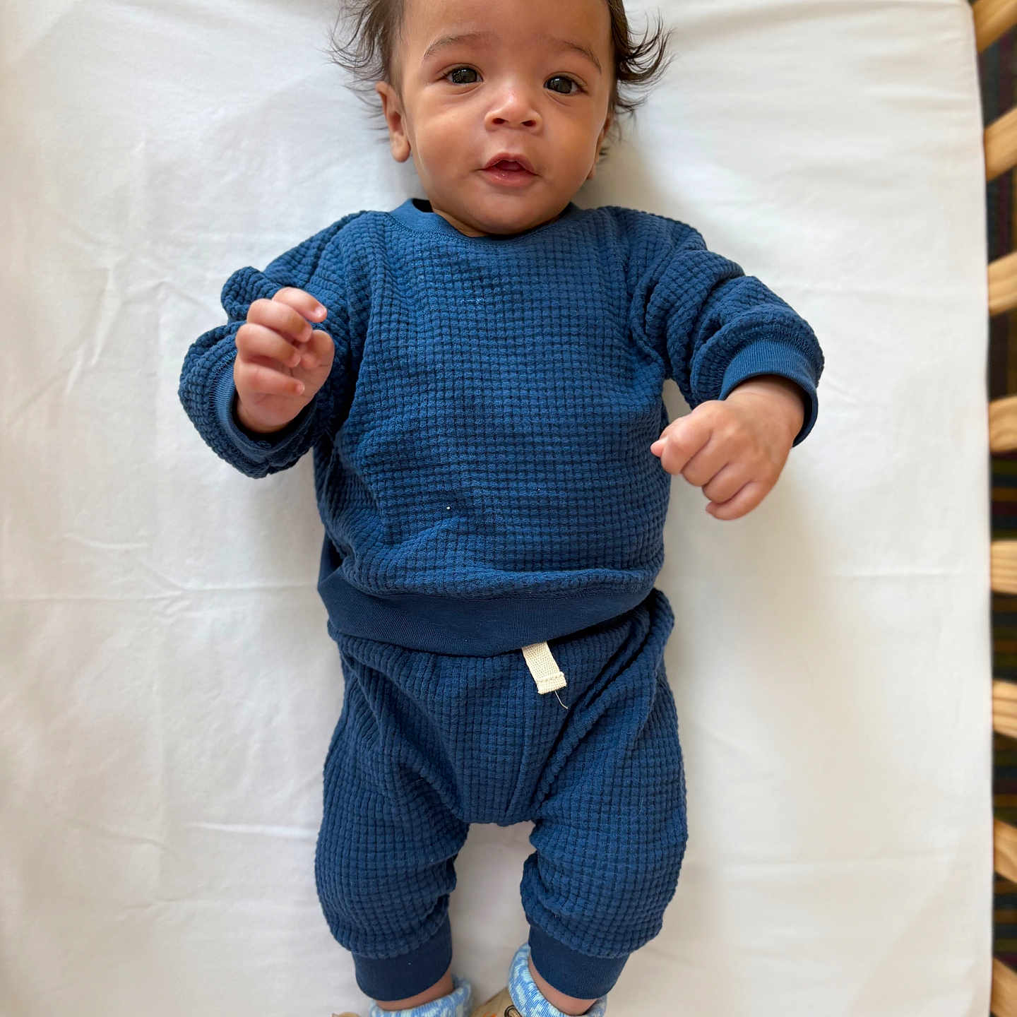 Javan Criswell joined the competition — help win amazing prizes! baby, infant, child, blue_outfit, sneakers, lying_down, white_sheet, curly_hair, portrait, cute, looking_at_camera, indoor, clothing, footwear, small_hands, infant_fashion, smiling, young_child, baby_boy, cozy