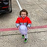 Adam is registered to the contest to win money with this photo: child, toddler, balloon, curly_hair, red_jacket, gray_jacket, sneakers, parking_lot, car, concrete, outdoor, smiling, holding, playful, young_child, sidewalk, street, vehicle, casual_clothing, daylight
