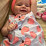 baby, child, smiling, headband, dress, patterned_clothing, toy, plush_toy, cushion, striped_fabric, indoor, cute, happy, infant, raised_arm, buttoned_dress, soft_toys, colorful, lying_down, portrait