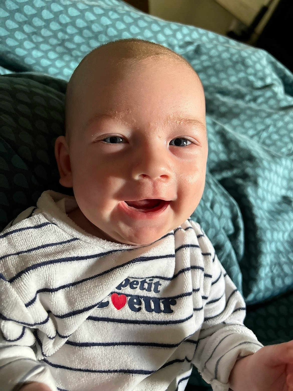Djuliane participe au concours pour gagner de l'argent avec cette photo : baby, bed, blanket, blue, child, clothing, cozy, cute, face, happy, head, indoor, infant, person, portrait, skin, smile, striped_shirt, text_on_clothing, young