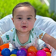 Jalen is registered to the contest to win money with this photo: baby, child, colorful_balls, outdoor, green_background, cushion, infant, playful, cute, portrait, short_hair, onesie, toy, happy, face, smiling, skin, young_child, daylight, closeup