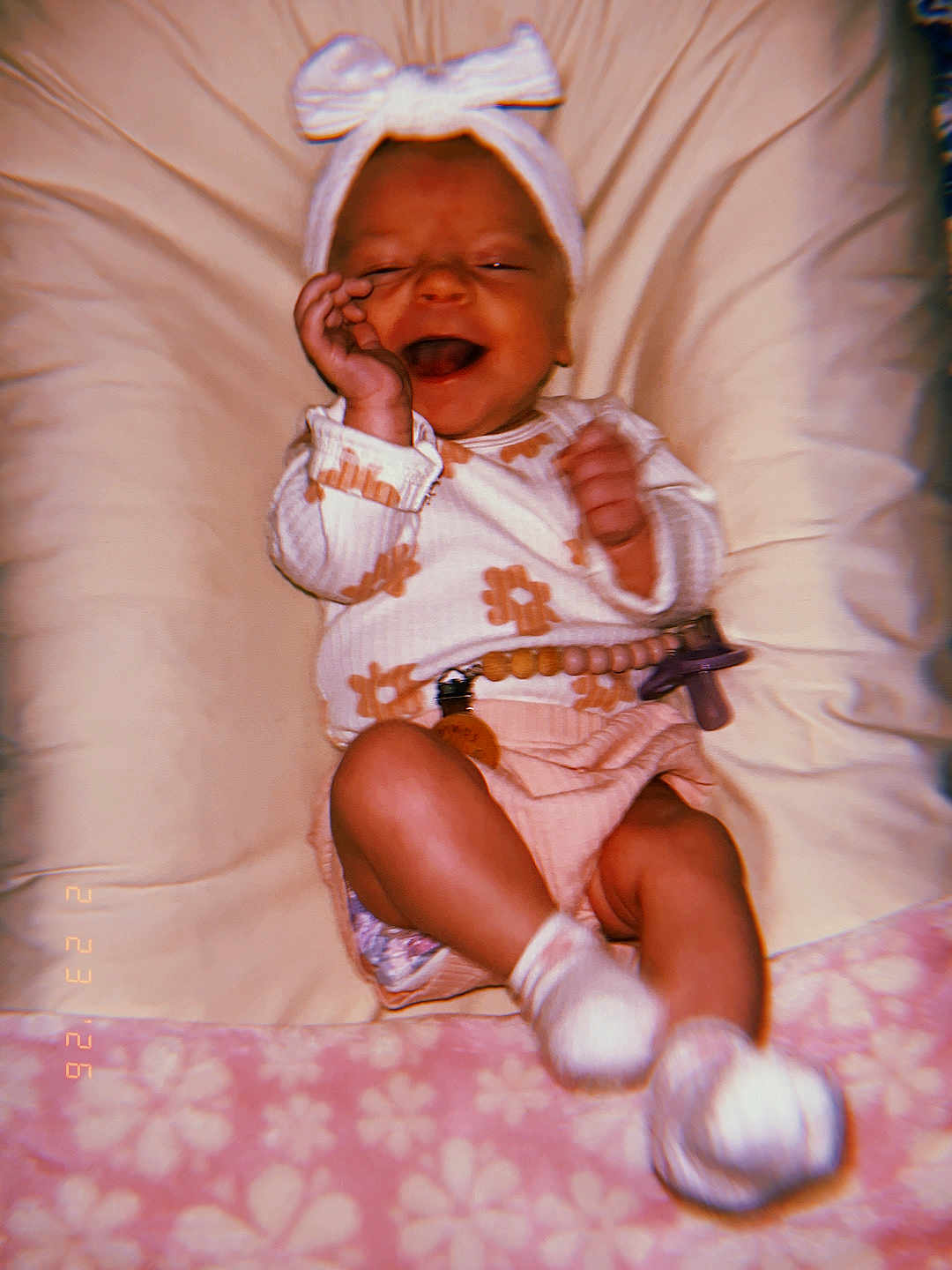 Isla is registered to the contest to win money with this photo: baby, infant, smiling, bow_headband, onesie, pacifier, pacifier_clip, blanket, bedding, cushion, socks, legs, hands, newborn, laughing, portrait, soft_texture, pink, floral_pattern, cozy