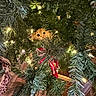 cat, christmas_tree, holiday_lights, greenery, decorations, orange_cat, curious, peeking, indoors, festive, twinkling_lights, pine_branches, hiding, wooden_floor, ornament, seasonal, holiday, cute, pet, feline
