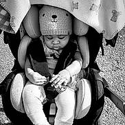 Alegend is registered to the contest to win money with this photo: baby, stroller, blanket, knit_hat, teddy_bear_pattern, child, outdoor, sunlight, toy, clothing, socks, seat_belt, infant, cute, peaceful, grayscale, portrait, person, small_object, warm_clothing