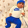 baby, blanket, blue_hat, blue_pants, child, clothing, cozy, cute, footed_pants, hat, indoor, infant, lying_down, nike_shirt, person, portrait, small_hands, soft_texture, teddy_bear_pattern, wide_eyes