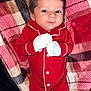 Santiago is registered to the contest to win money with this photo: baby, infant, red_onesie, mittens, plaid_blanket, cozy, sleepwear, cute, newborn, child, lying_down, warm, white_socks, pattern, soft_texture, portrait, indoor, small_feet, face, young