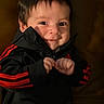Santiago is registered to the contest to win money with this photo: baby, black_clothing, child, closeup, cozy, cute, expression, face, hands, human, indoor, infant, jacket, mischievous, person, portrait, red_stripes, smile, warm_lighting, young_child