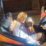 Kenzo participe au concours pour gagner de l'argent avec cette photo : adult, amusement_park, blonde_hair, bumper_car, casual_clothing, child, dark_background, fun, hand_gesture, leisure, lighting, night, outdoor, peace_sign, person, ride, seat, shadow, smile, vehicle