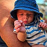 Jaxon is registered to the contest to win money with this photo: baby, infant, child, portrait, sunhat, blue_hat, striped_shirt, barefoot, toes, hands, sitting, held, adult_arm, outdoor, sunlight, close_up, face, serious_expression, clothing, family