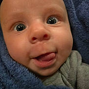 Jaxon joined the competition — help win amazing prizes! baby, infant, child, face, portrait, close_up, eyes, tongue, smiling, curious, blanket, wrapped, blue, clothing, indoors, cozy, sitting, head, skin, photography
