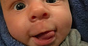 Jaxon joined the competition — help win amazing prizes! baby, blanket, blue, child, close_up, clothing, cozy, curious, eyes, face, head, indoors, infant, photography, portrait, sitting, skin, smiling, tongue, wrapped