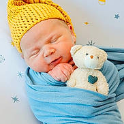 Hudson is registered to the contest to win money with this photo: baby, background_pattern, blue_wrap, child, cozy, cute, face, hand, indoors, infant, newborn, peaceful, plush_toy, portrait, sleeping, soft_texture, star_pattern, teddy_bear, wrapped, yellow_hat